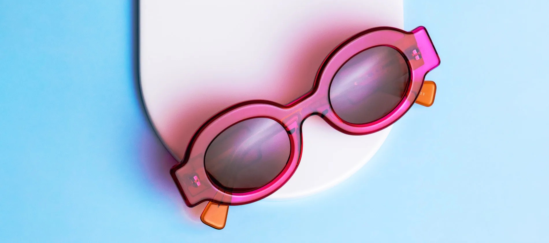 Pink round Anne & Valentin sunglasses with orange temples on a blue background