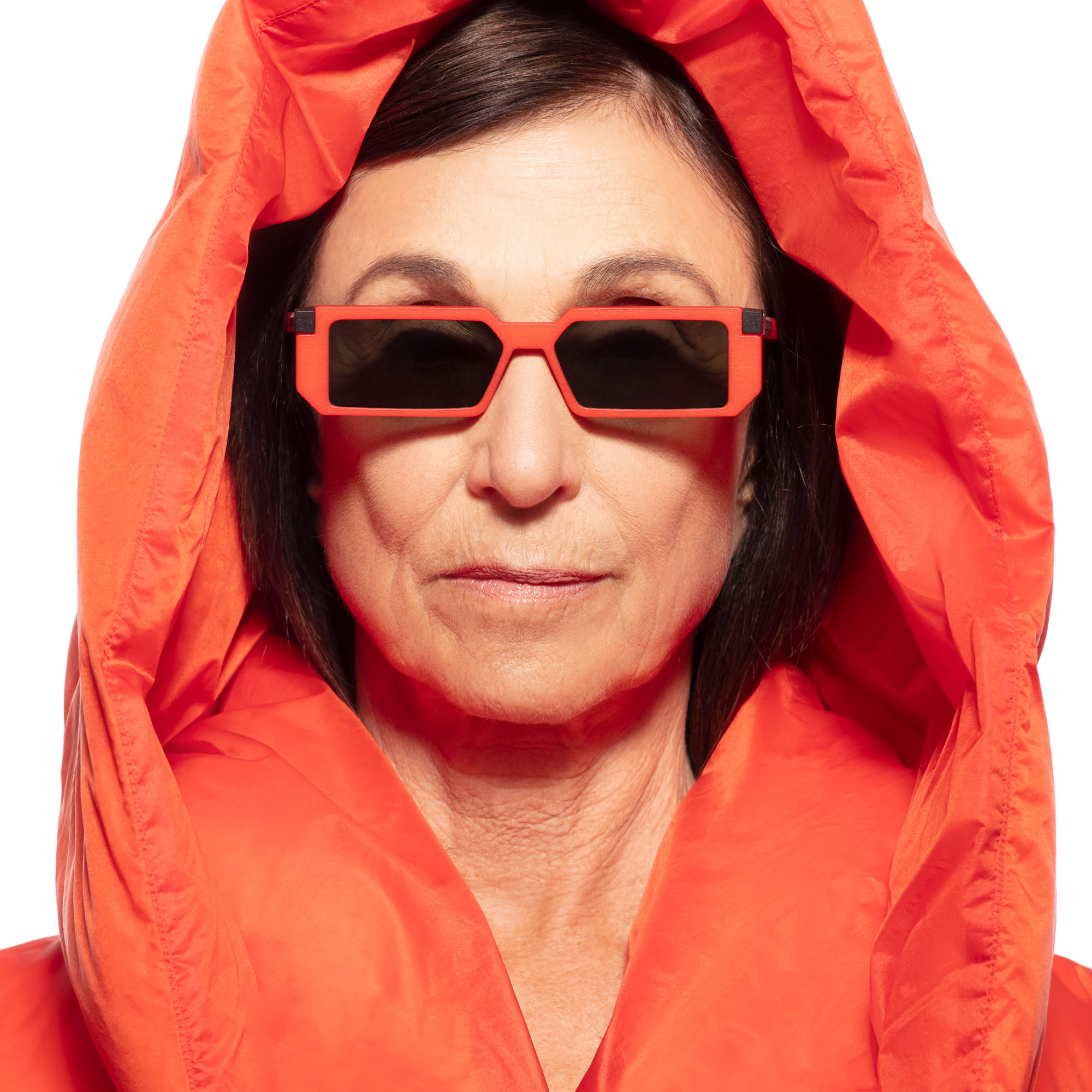A woman in an orange hood wearing rectangular orange VAVA sunglasses, close-up portrait